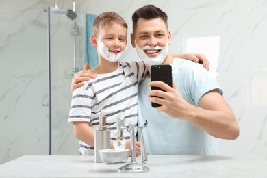 Son and dad with shaving foam on faces taking selfie in bathroom