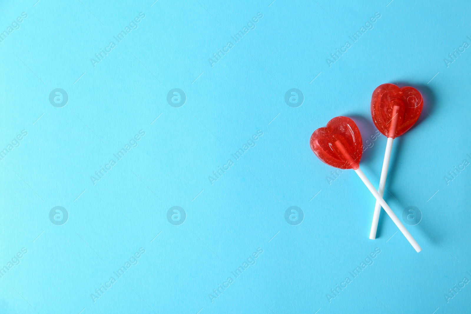 Photo of Heart shaped lollipops and space  text  color background, top view. Sweet love