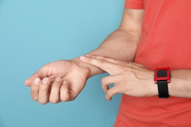 Photo of Young man checking pulse on color background, closeup