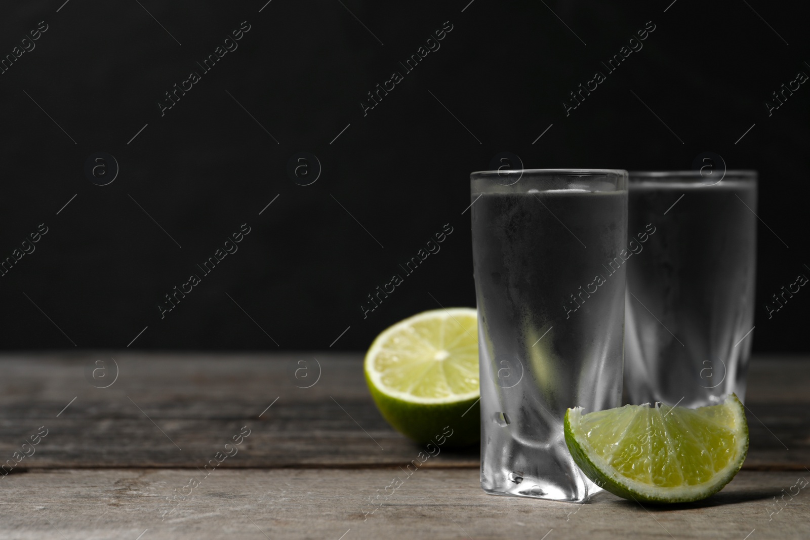 Photo of Shot glasses of vodka with lime on wooden table. Space for text