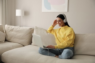 Photo of Woman with laptop and headphones sitting on sofa at home