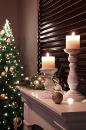 Photo of Burning candles and Christmas decor on white mantelpiece