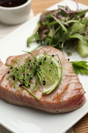 Photo of Delicious tuna steak with microgreens and lime on plate, closeup