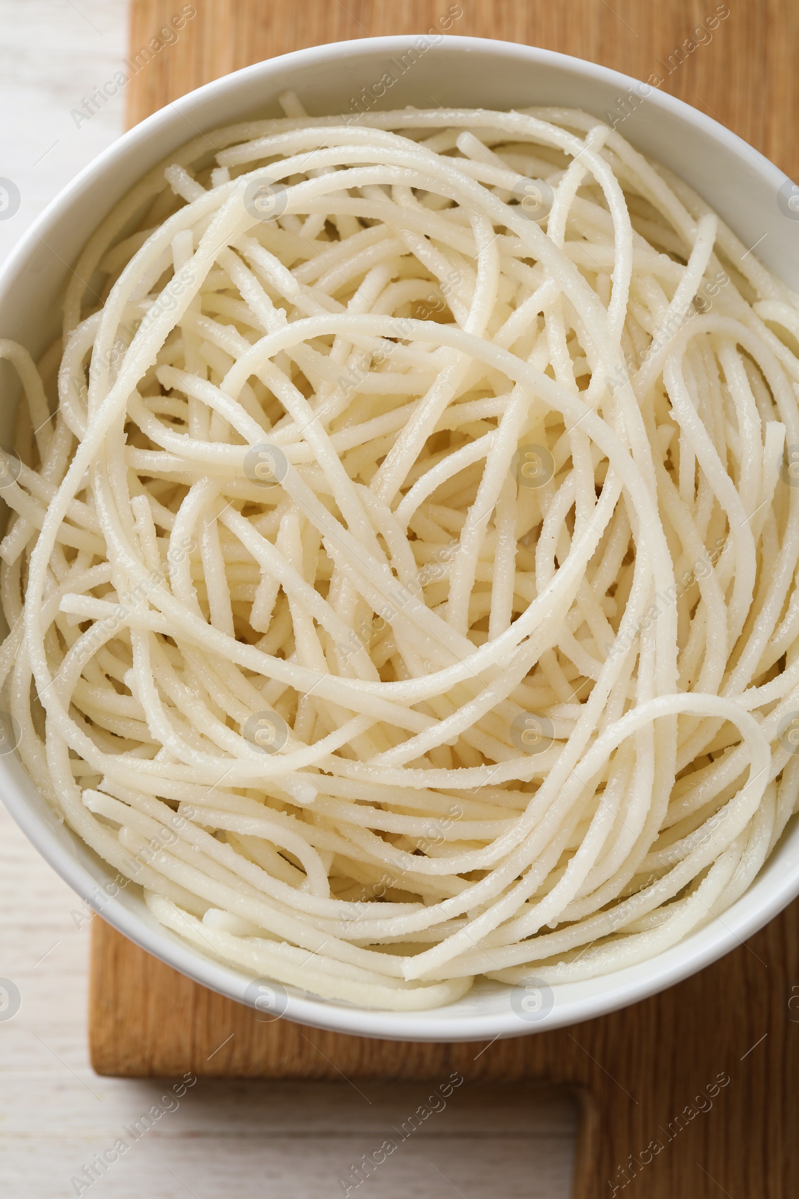 Photo of Bowl of tasty cooked rice noodles on white wooden table, top view