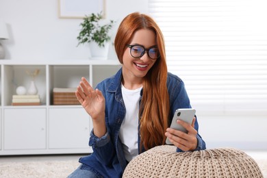Photo of Happy young woman waving hello during video chat via smartphone at home
