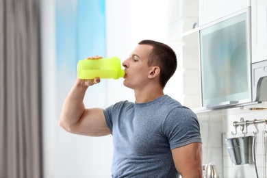 Photo of Athletic young man drinking protein shake in kitchen