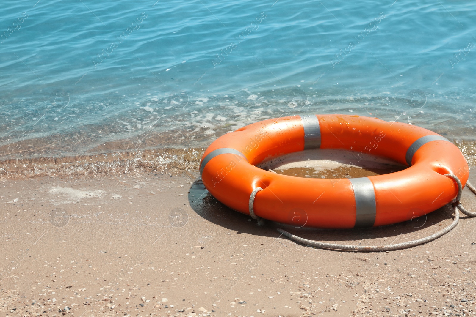 Photo of Orange life buoy on sand near sea. Emergency rescue equipment