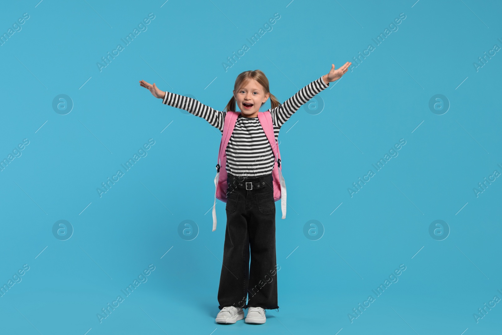 Photo of Happy schoolgirl with backpack on light blue background