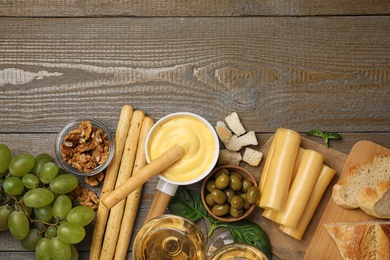 Flat lay composition with pot of tasty cheese fondue and products on wooden table, space for text