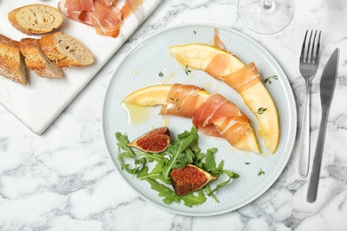 Flat lay composition with plate of melon slices and prosciutto on marble table