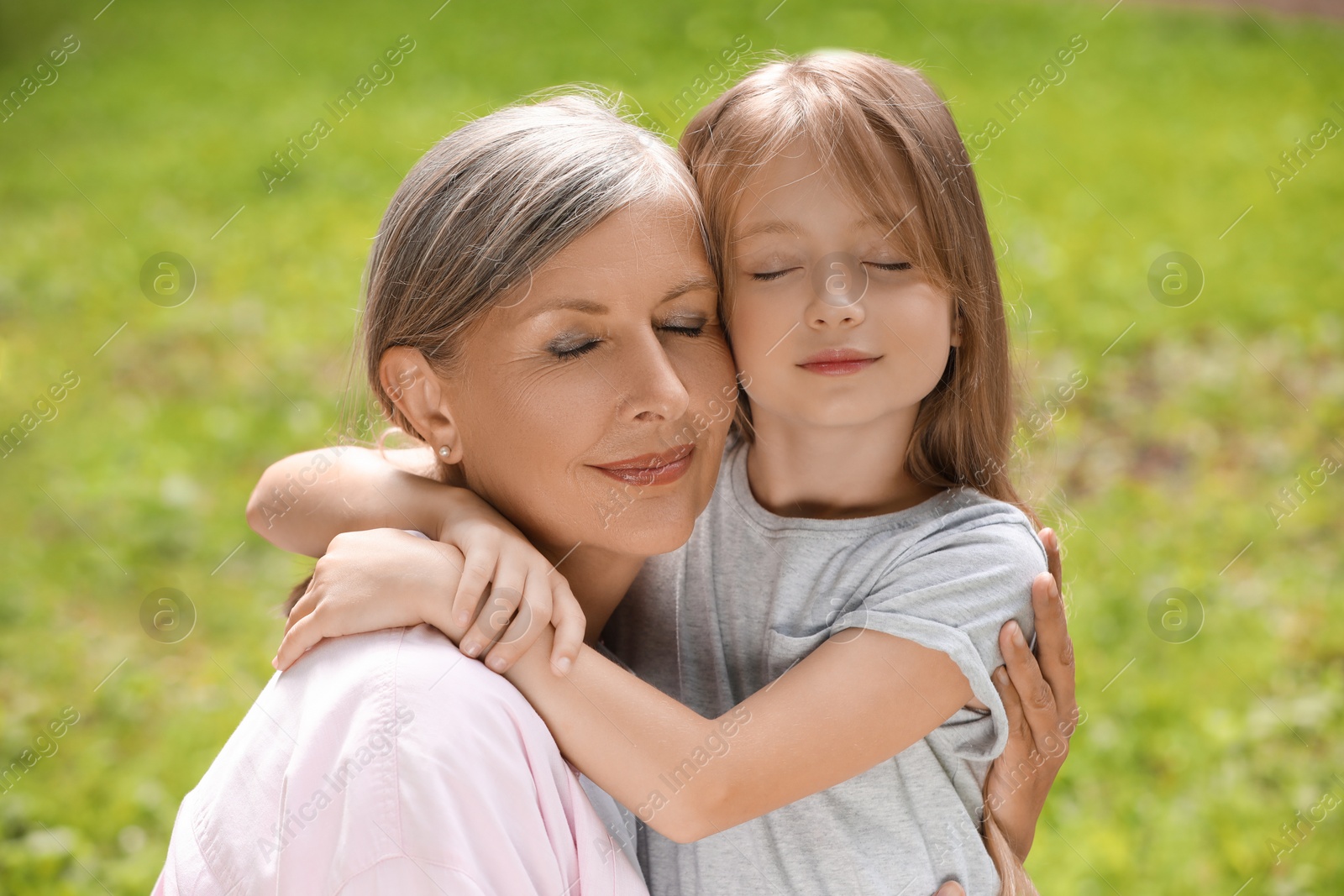 Photo of Portrait of happy grandmother hugging her granddaughter outdoors