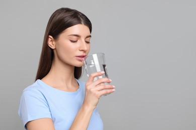 Healthy habit. Woman drinking fresh water from glass on grey background. Space for text