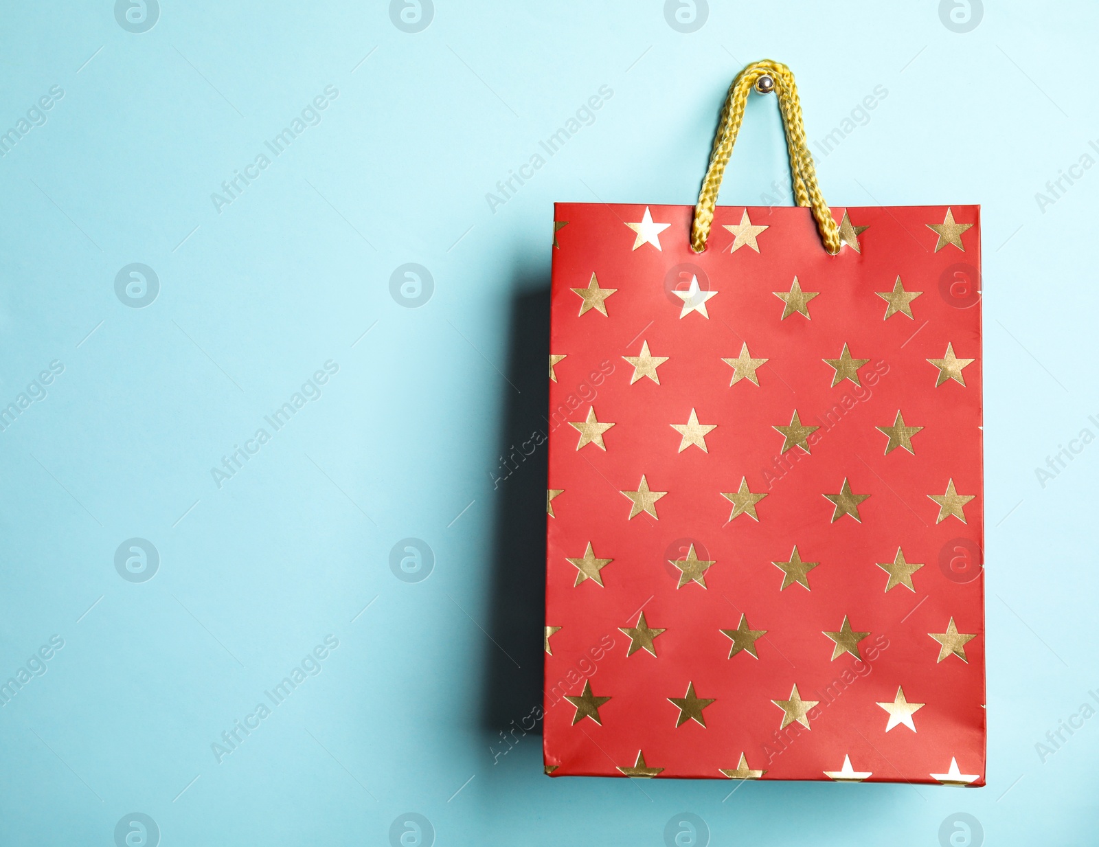 Photo of Red shopping paper bag with star pattern on light blue background, space for text