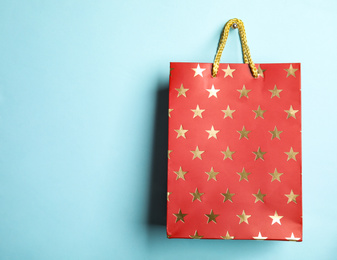 Photo of Red shopping paper bag with star pattern on light blue background, space for text