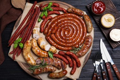 Different delicious sausages with herbs and sauces on black wooden table, flat lay. Assortment of beer snacks