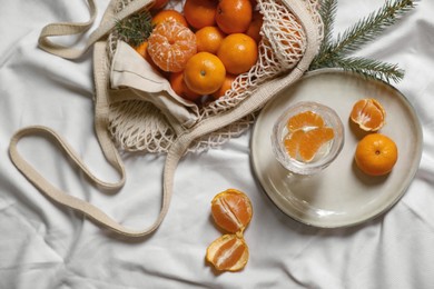 Photo of Delicious ripe tangerines, glass with sparkling wine and fir branch on white bedsheet, flat lay