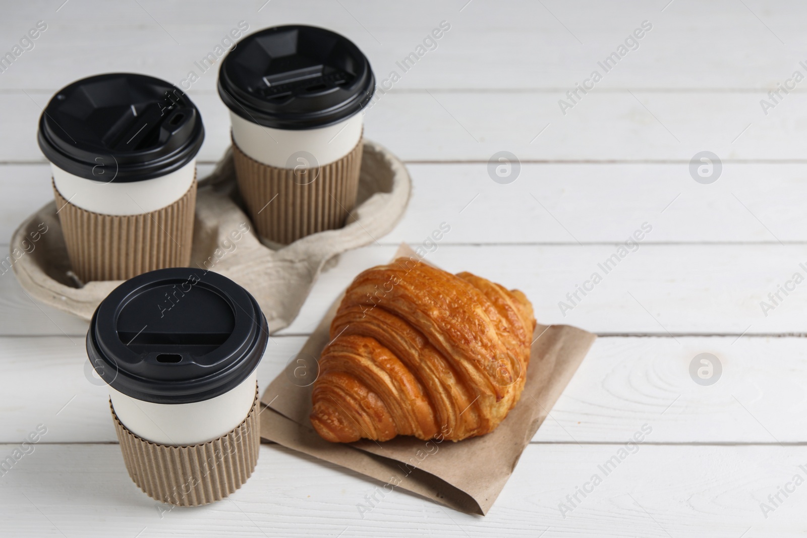 Photo of Coffee to go. Paper cups with tasty drink and croissant on white wooden table. Space for text