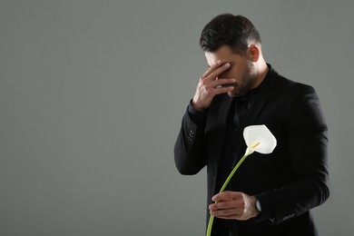 Sad man with calla lily flower mourning on grey background, space for text. Funeral ceremony