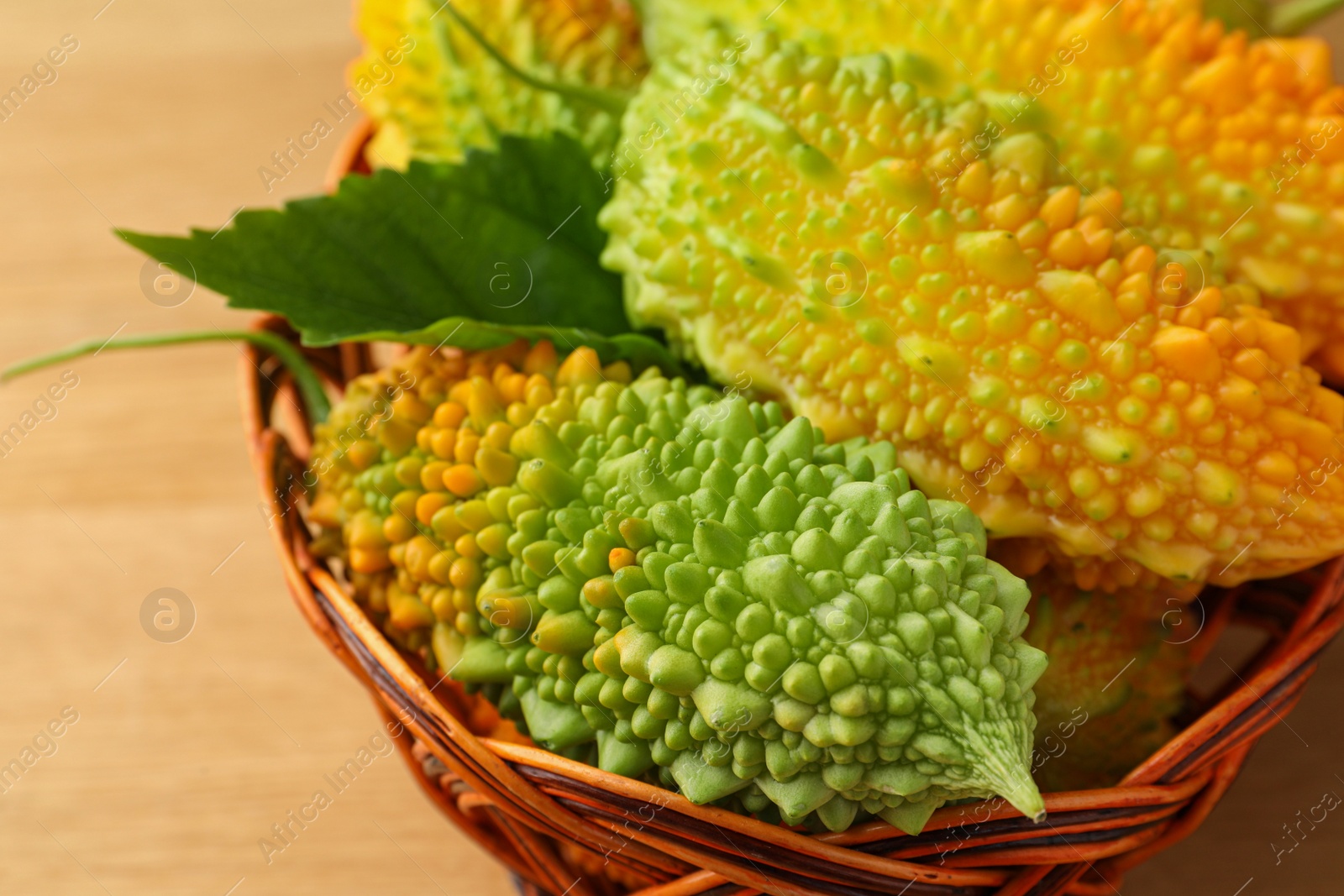 Photo of Basket with fresh bitter melons on wooden table, closeup