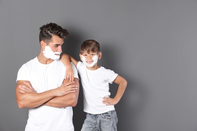 Photo of Father and son with shaving foam on faces against color background. Space for text