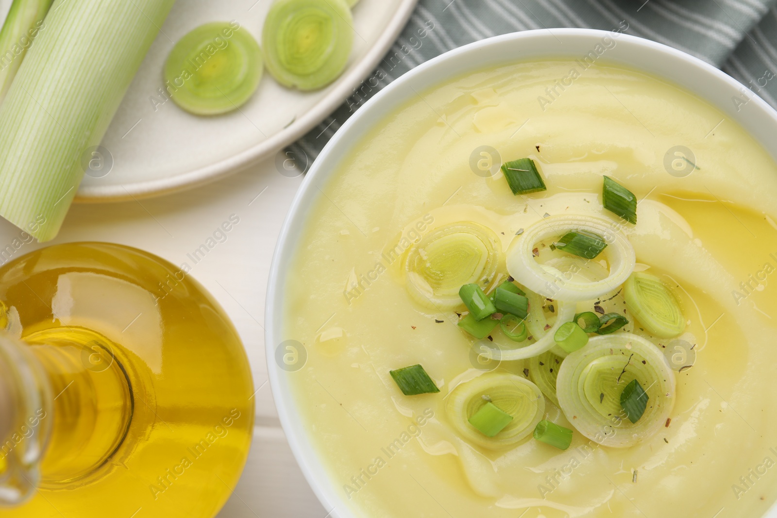 Photo of Bowl of tasty cream soup with leek on wooden table, flat lay
