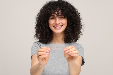 Photo of Young woman holding teeth whitening strips on light grey background