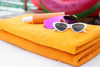 Beach towels, sunglasses and sunscreen on sunbed near outdoor swimming pool. Luxury resort