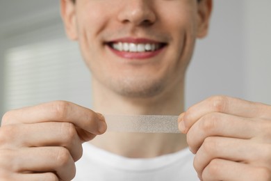 Young man with whitening strip indoors, closeup