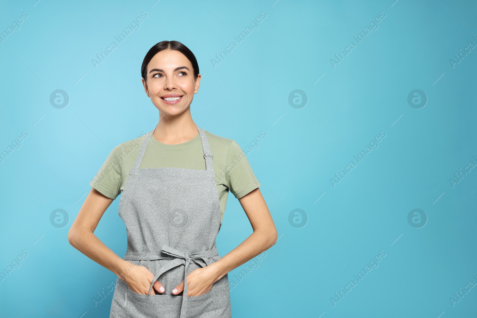 Photo of Young woman in grey apron on light blue background, space for text