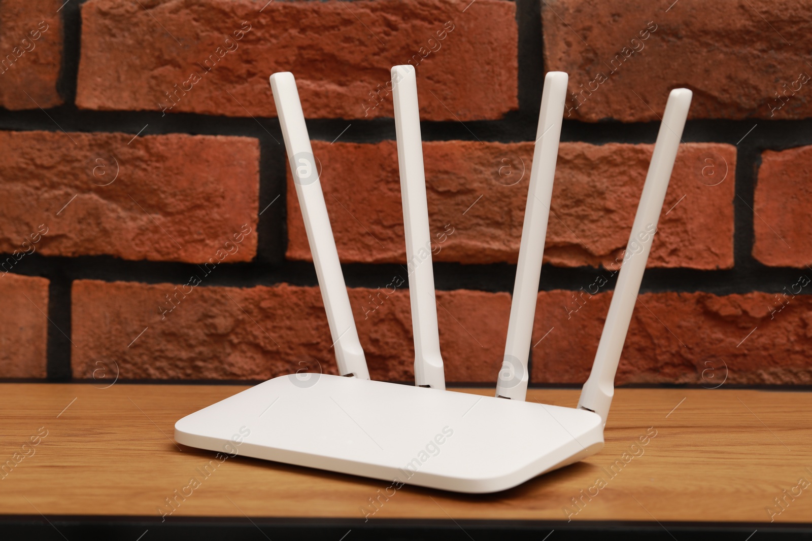 Photo of New white Wi-Fi router on wooden table near brick wall