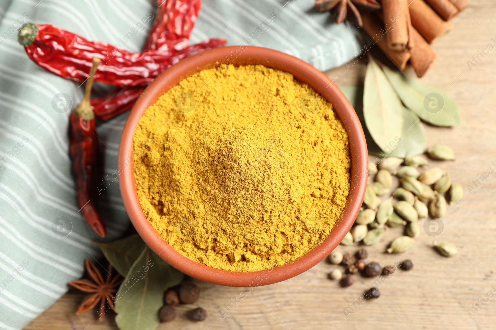 Photo of Curry powder in bowl and other spices on wooden table, flat lay