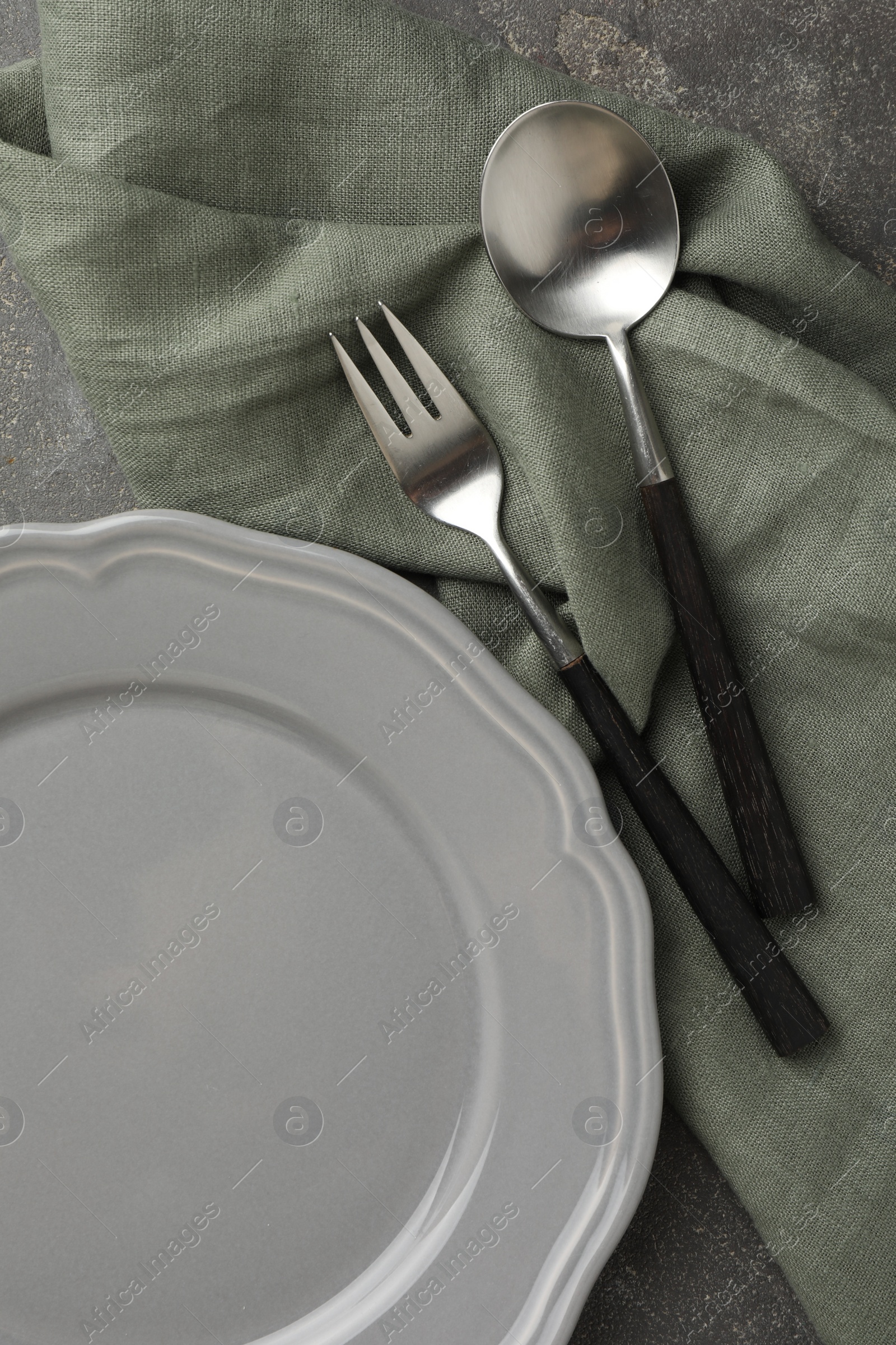 Photo of Stylish setting with cutlery, napkin and plate on grey textured table, top view