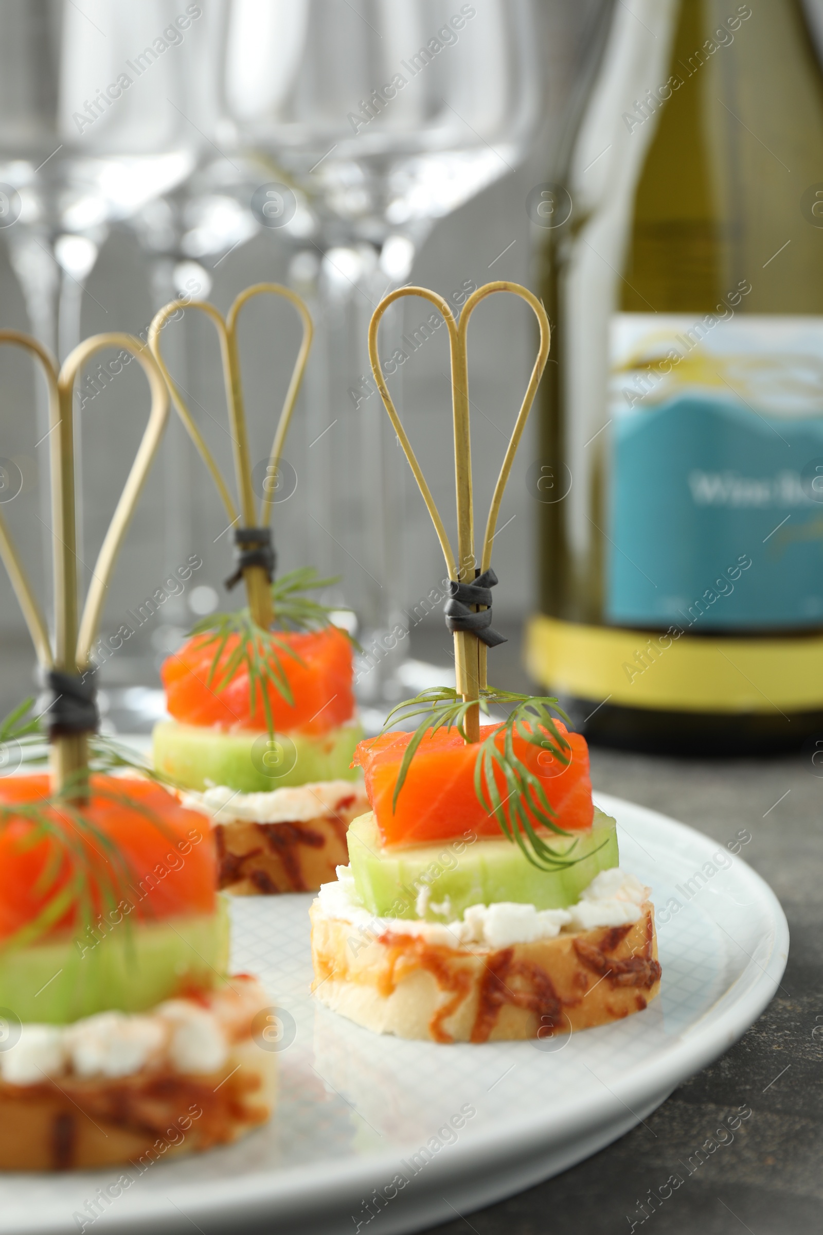 Photo of Tasty canapes with salmon, cucumber, bread and cream cheese on grey table, closeup