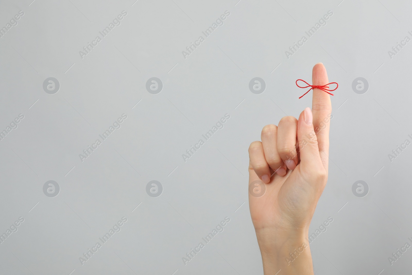 Photo of Woman showing index finger with tied red bow as reminder on light grey background, closeup. Space for text