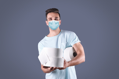 Image of Man in medical mask holding toilet paper rolls on grey background