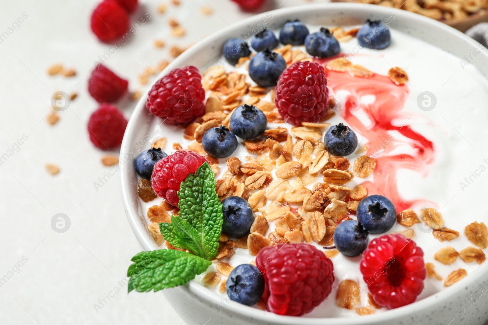 Photo of Tasty homemade granola with yogurt and berries on light table, closeup. Healthy breakfast