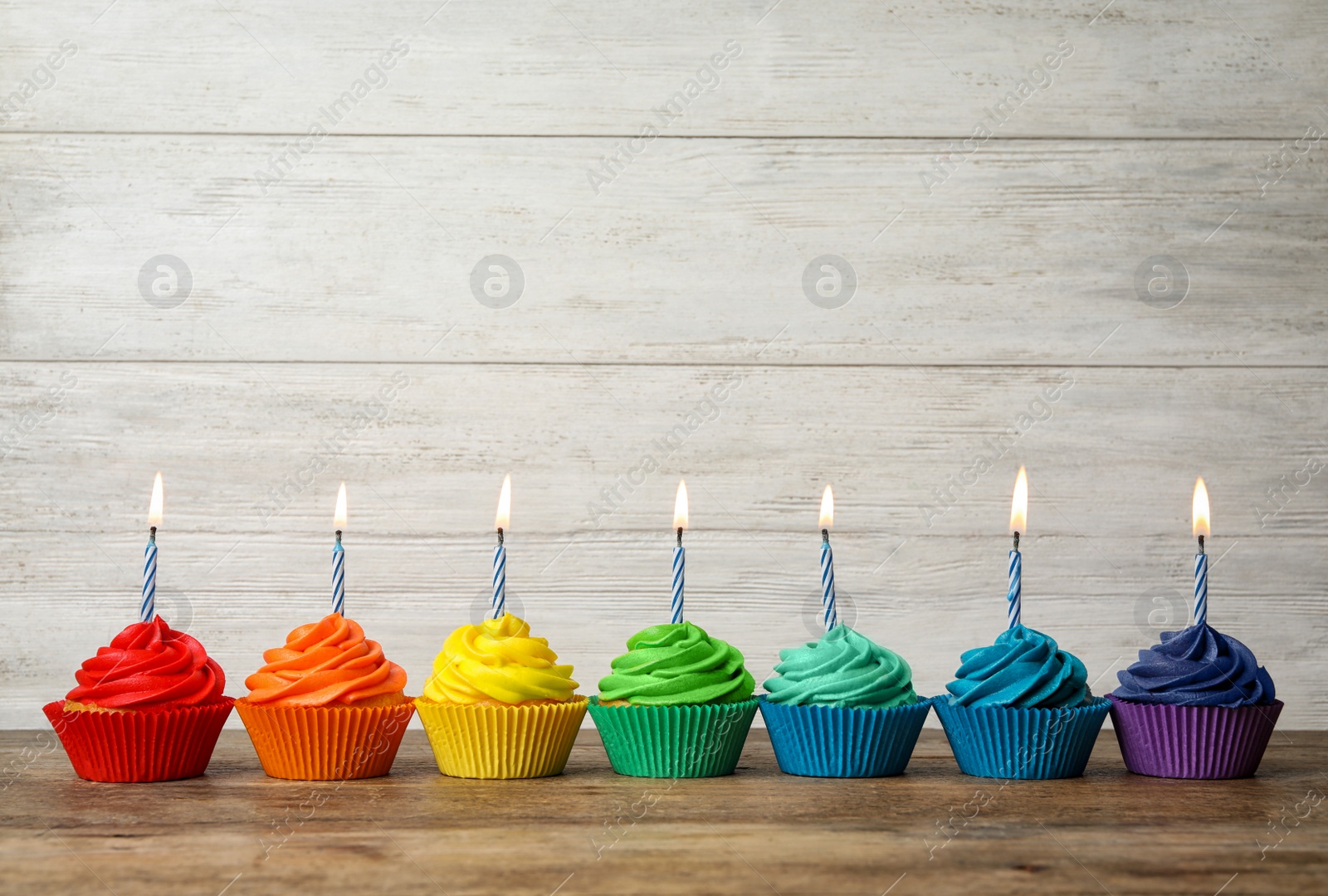 Photo of Delicious birthday cupcakes with burning candles on wooden table