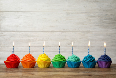 Photo of Delicious birthday cupcakes with burning candles on wooden table