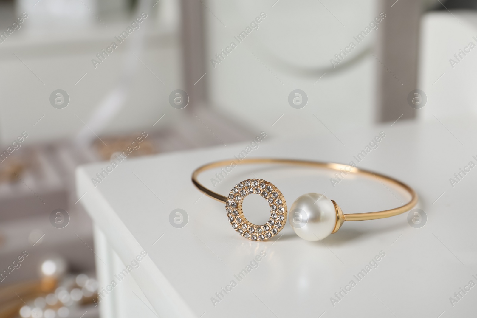 Photo of Elegant golden bracelet with pearl and diamonds on white table, closeup view