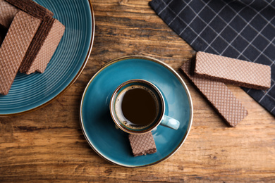 Photo of Delicious wafers and cup of coffee for breakfast on wooden table, flat lay