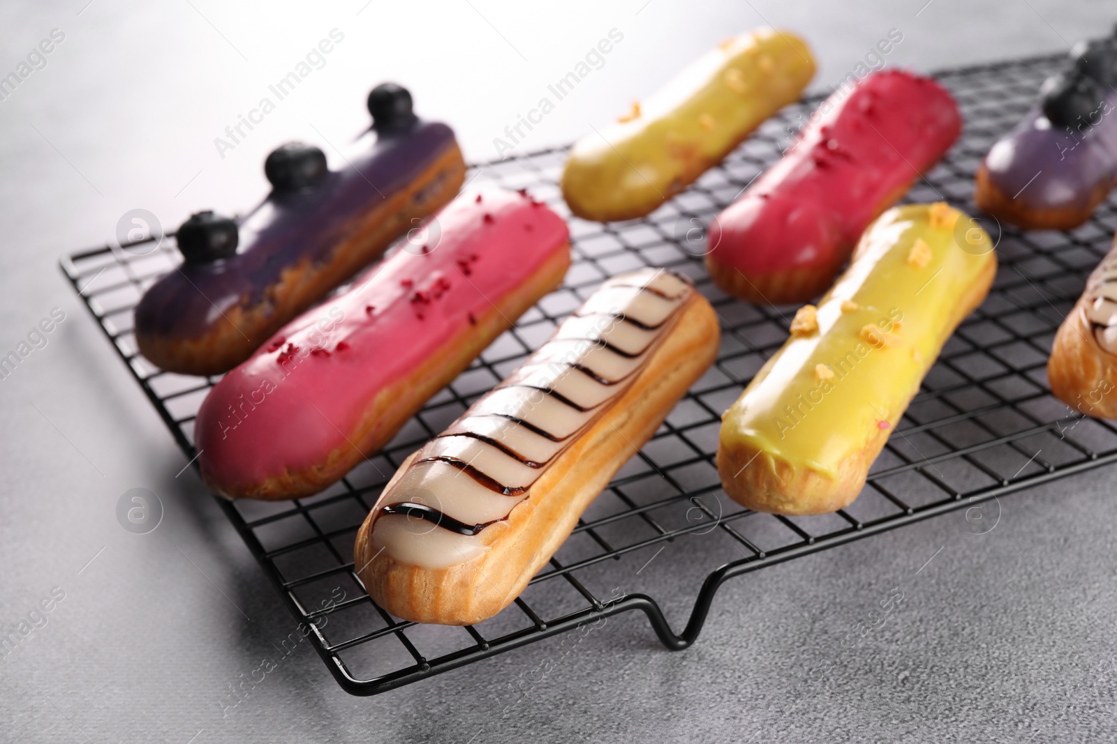 Photo of Cooling rack with different tasty glazed eclairs on grey table, closeup