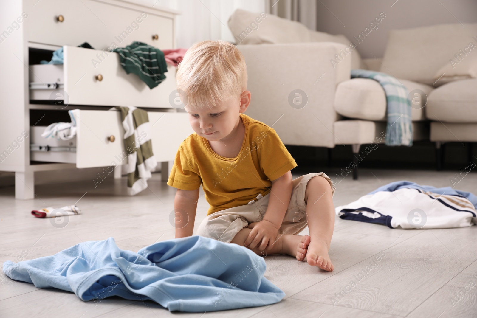 Photo of Cute little boy sitting on floor in messy room