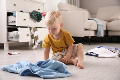 Photo of Cute little boy sitting on floor in messy room