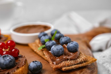 Photo of Fresh crunchy rye crispbreads with chocolate spread and blueberries on wooden board, closeup