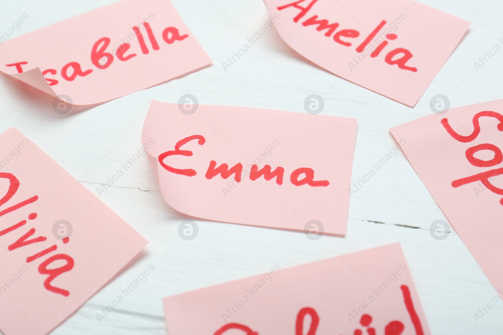 Photo of Paper stickers with different names on white wooden table, closeup. Choosing baby's name