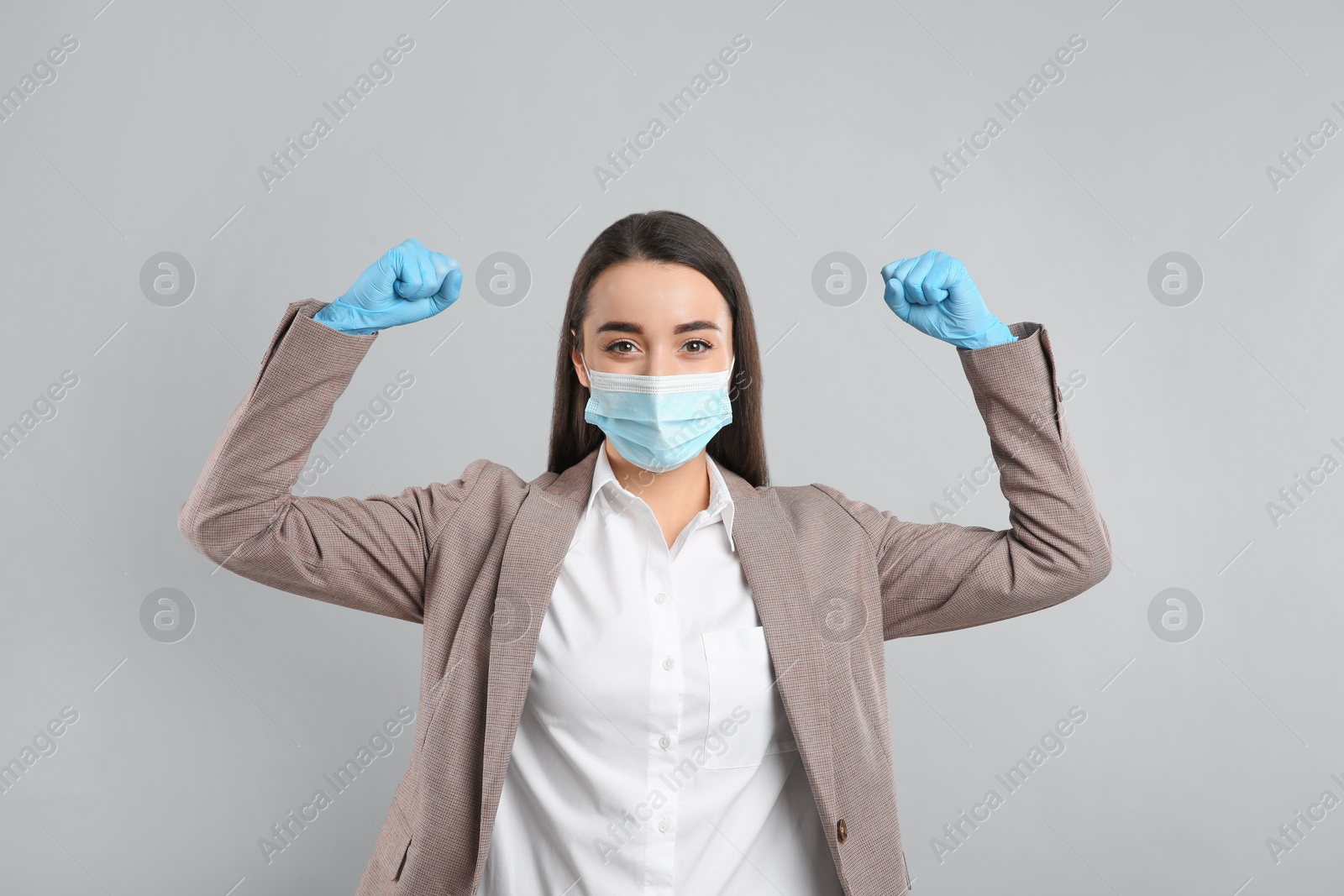 Photo of Businesswoman with protective mask and gloves showing muscles on light grey background. Strong immunity concept
