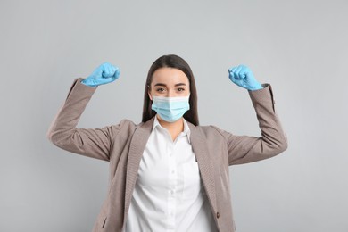 Businesswoman with protective mask and gloves showing muscles on light grey background. Strong immunity concept