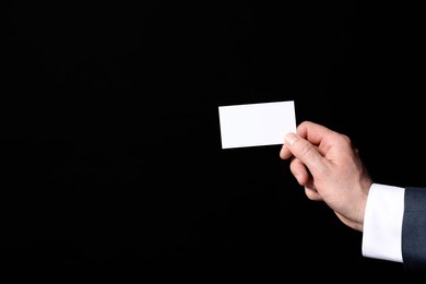 Businessman holding blank business card on black background, closeup. Space for text