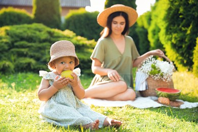 Photo of Mother and her daughter having picnic in garden, focus on baby with apple