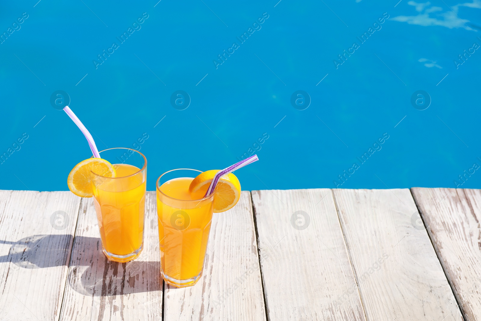 Photo of Refreshing cocktails near outdoor swimming pool on sunny day. Space for text